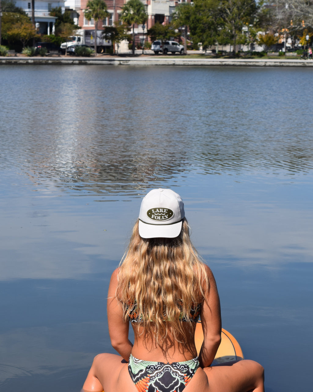 Woman sitting on a surfboard in a flat lake with a cityscape in the background